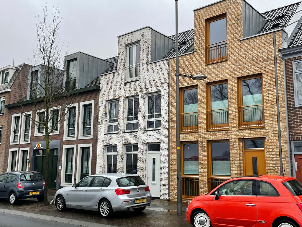 Smalle nieuwbouwwoningen tussen bestaande panden: een wit gekeimde gevel tussen zandkleurig en geel metselwerk