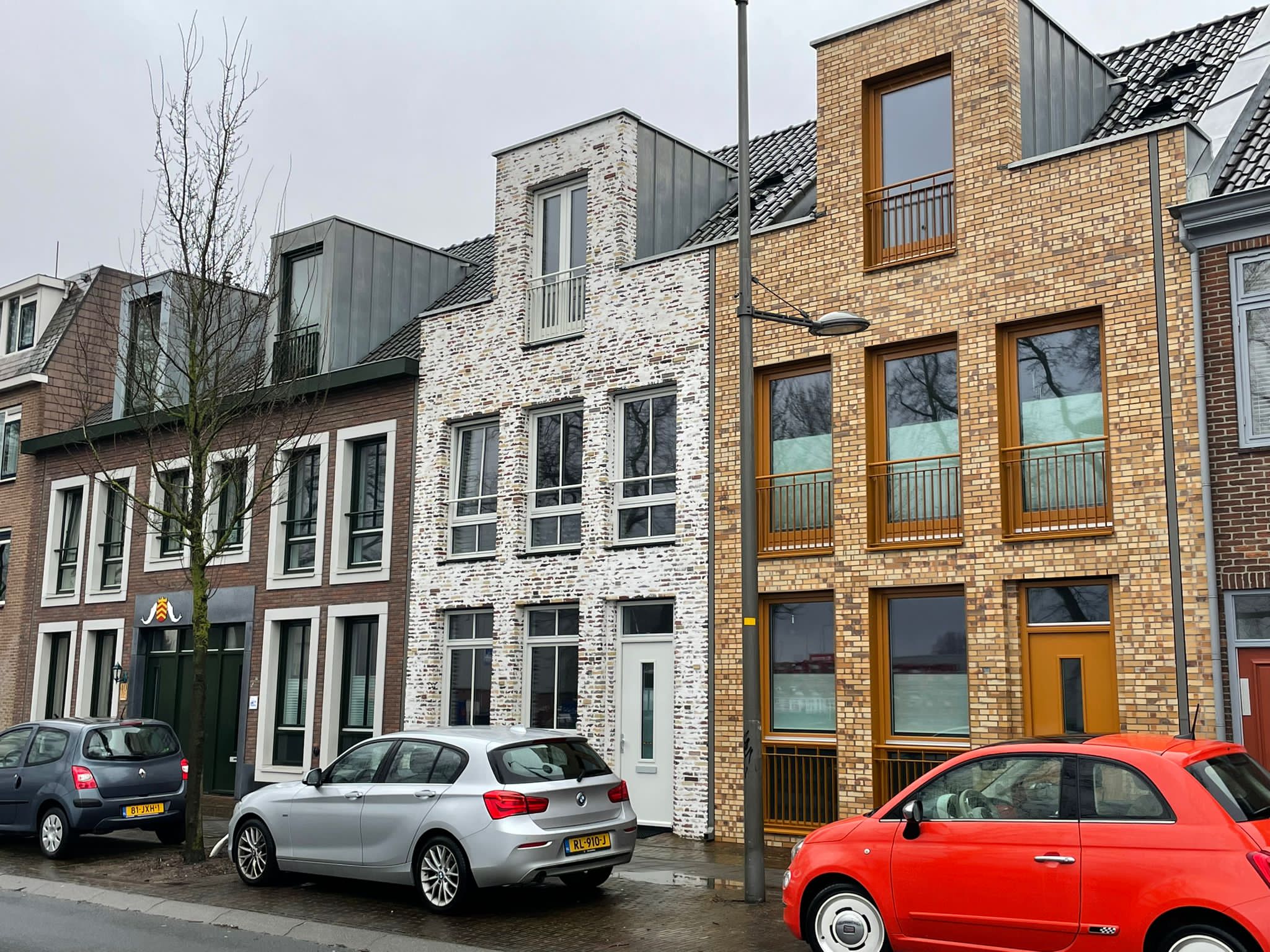 Smalle nieuwbouwwoningen tussen bestaande panden: een wit gekeimde gevel tussen zandkleurig en geel metselwerk
