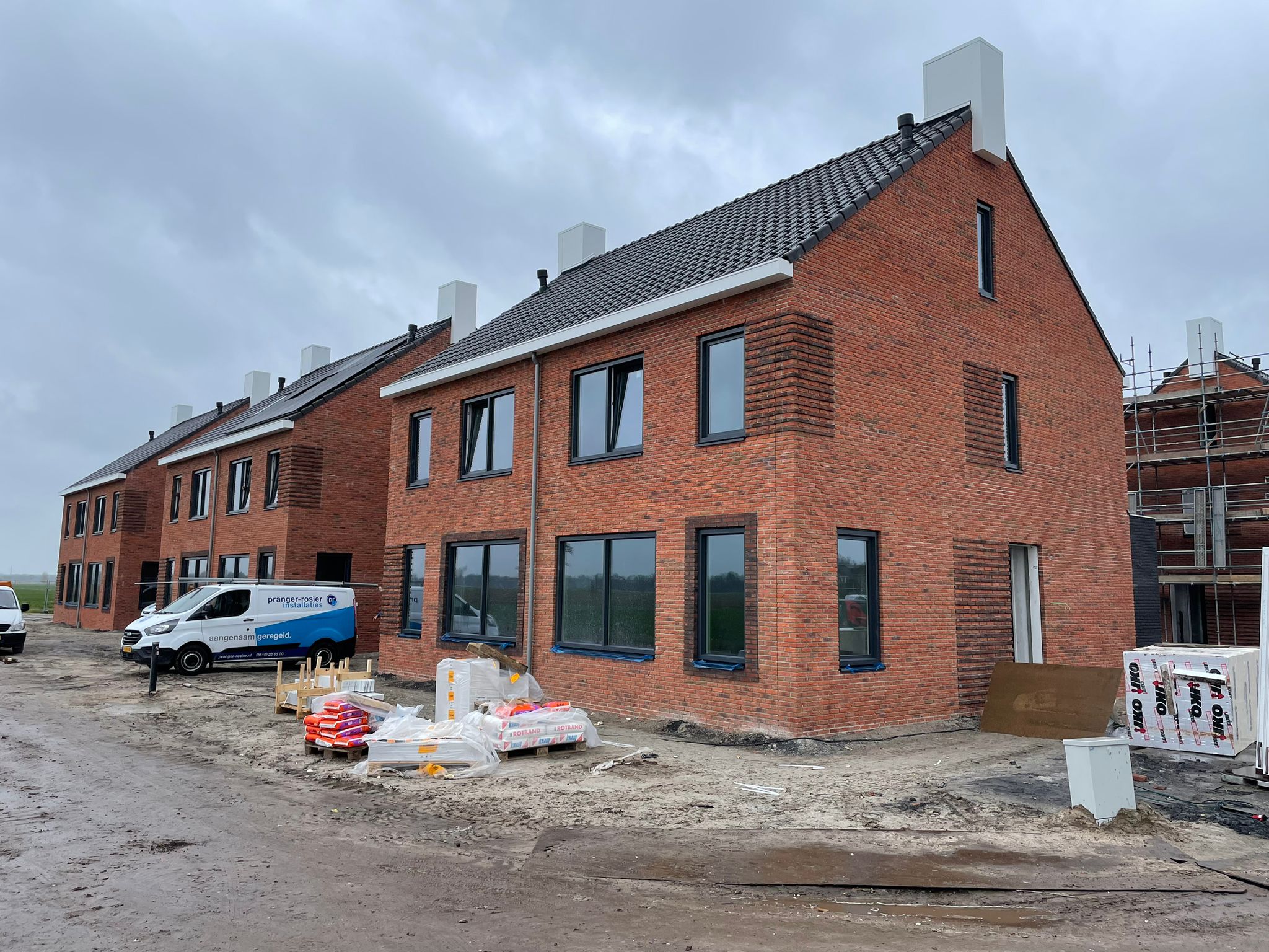 Rij nieuwbouwwoningen in rode baksteen, vrijwel gereed