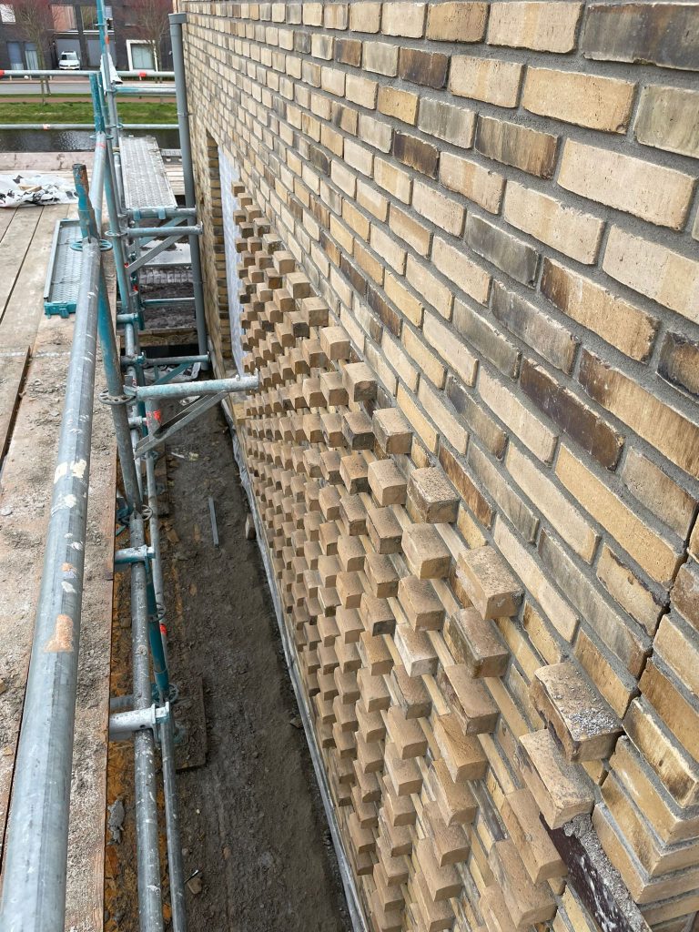 Detail van uitkragend metselwerk dat als reliëfband langs de gevel omhoogloopt