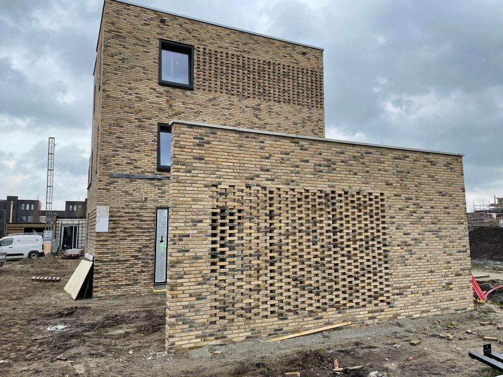 Lichte baksteengevel met een groot opengewerkt siermetselwerkpaneel in de kopgevel