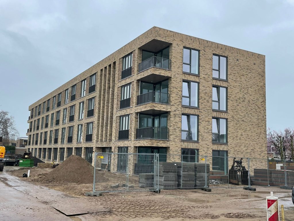 Appartementengebouw van vier lagen in lichte baksteen, gezien vanaf de bouwplaats