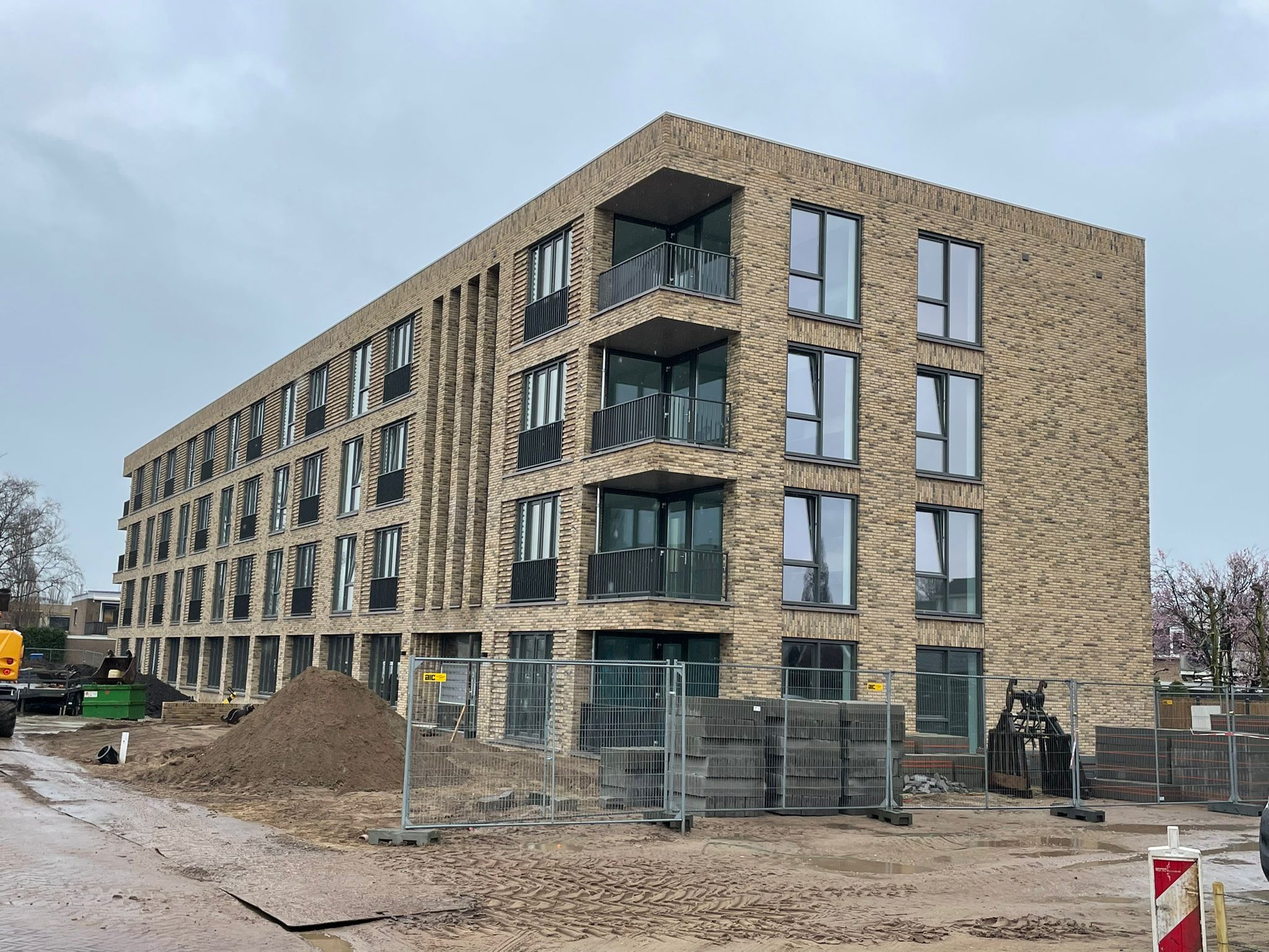 Appartementengebouw van vier lagen in lichte baksteen, gezien vanaf de bouwplaats