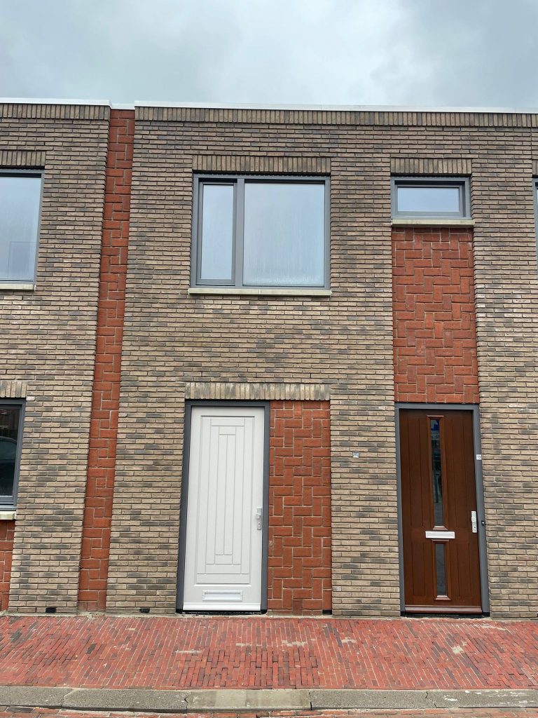 Gevelvak met rode baksteenpenanten rond een lichtgemetseld vlak met deur en raam