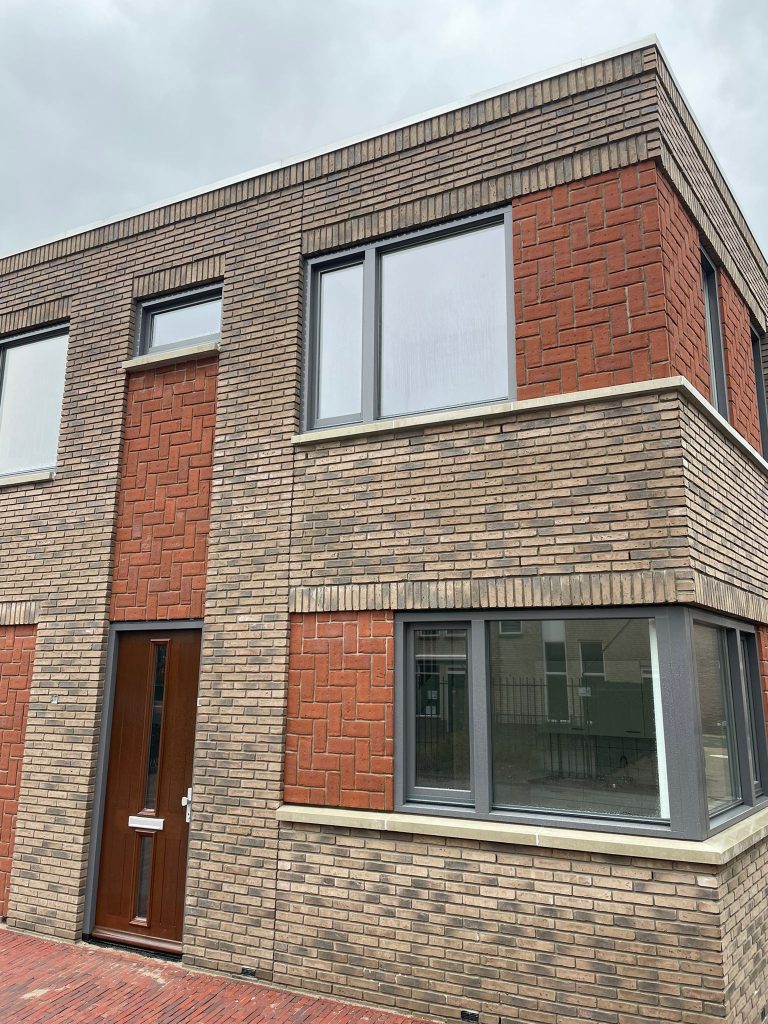 Detail van de hoek: licht metselwerk met rode banden en een uitkragende steenlaag