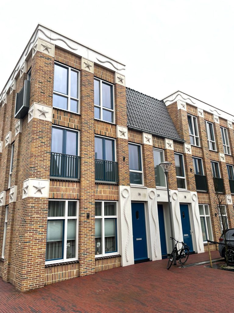 Hoekgevel van de nieuwbouwwoningen met blauwe voordeuren en witte muurankers