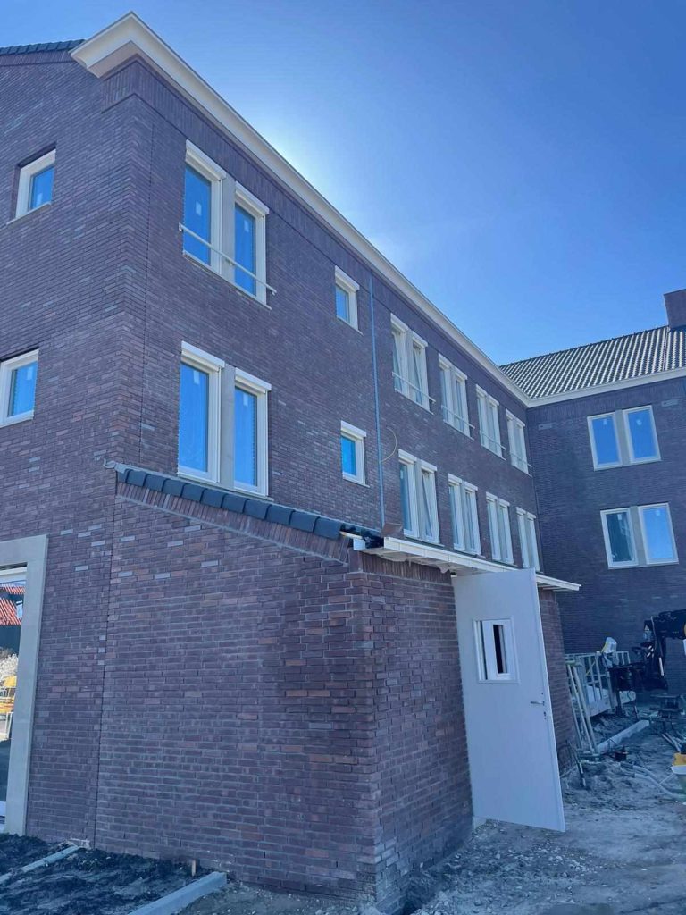 Achterzijde met een lager bouwdeel in rode baksteen en een dienstdeur, tijdens de afbouw