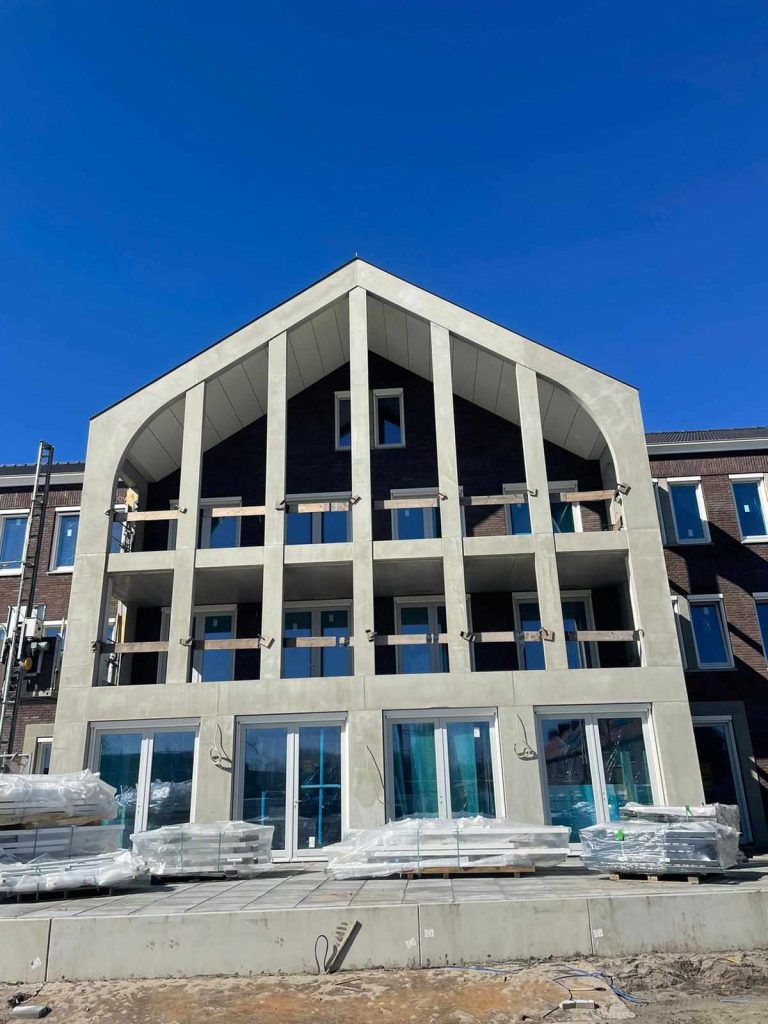 Betonnen puntgevel met staande lamellen en balkons, met verpakte bouwmaterialen op het terras ervoor