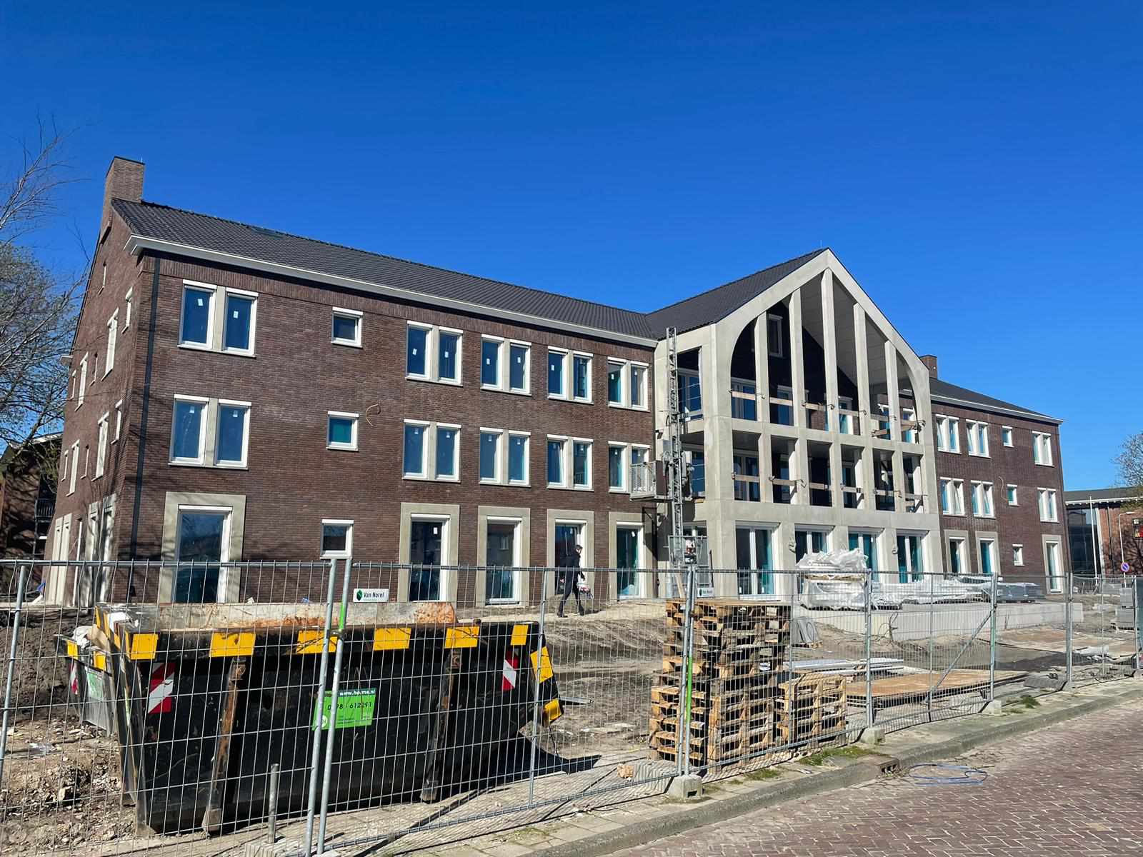Het gebouw in de afbouwfase: donkere baksteen, een betonnen puntgevel met balkons en bouwhekken op de voorgrond