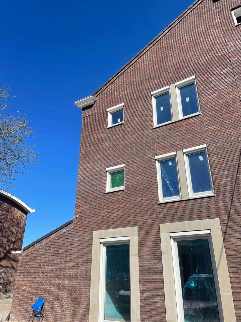 Zijgevel in rode baksteen onder een witte daklijst, met omlijste glazen deuren op de begane grond