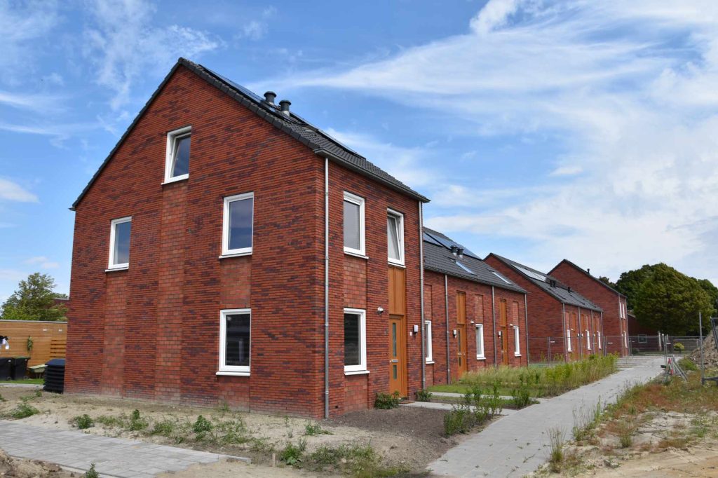 Nieuwe rij woningen in rode baksteen met houten voordeuren, gezien langs de kopgevel