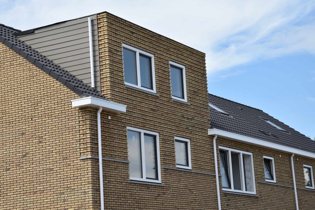 Gevel van gele baksteen met witte kozijnen, een dakkapel en een pannendak